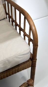 Close-up of a rustic rattan armchair with beige cushion on a white background.