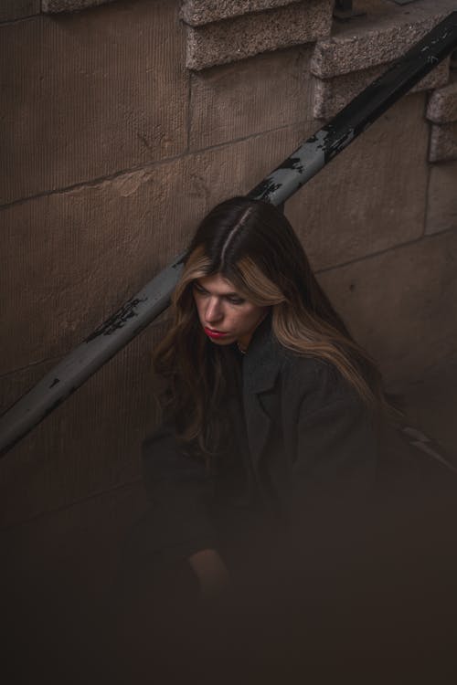 Woman in Coat Sitting by Handrail