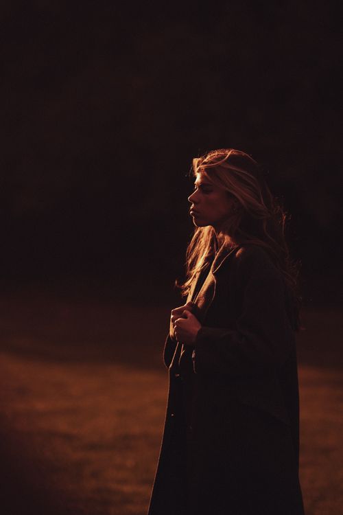 Free A woman in a coat stands in a sunlit rural setting, highlighting her profile. Stock Photo