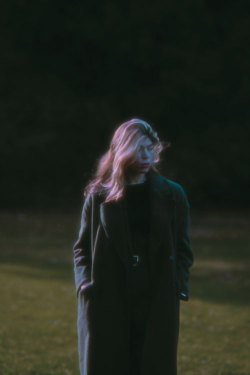 Free A contemplative portrait of a woman in a long coat, captured in a serene outdoor setting. Stock Photo