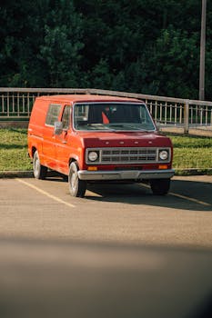 A vintage red Ford E-150 van parked outdoors on a sunny day, showcasing classic design.