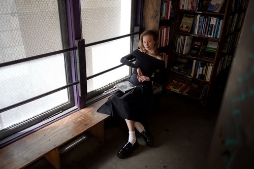 Free A woman sits elegantly by the window in a vintage bookshop, surrounded by books, enjoying a peaceful moment. Stock Photo