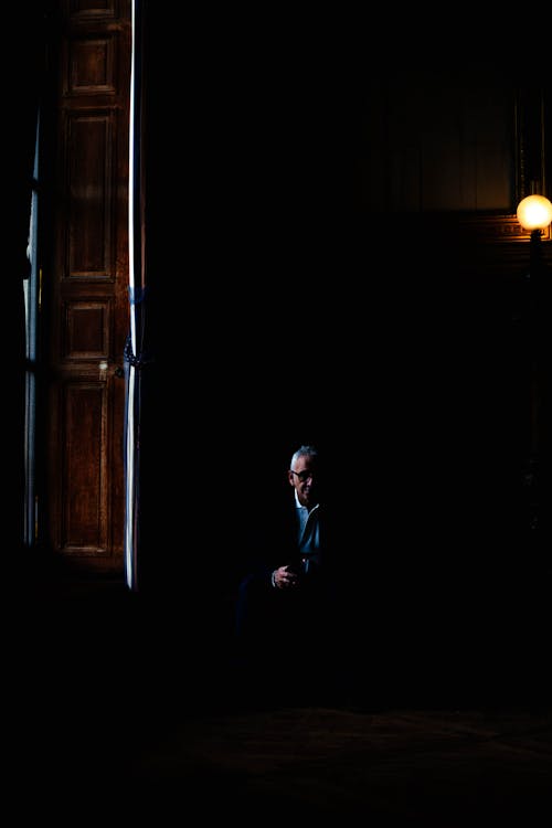 Elderly Man Sitting in Darkness in Room