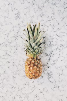 A vibrant pineapple on a minimalist marble texture surface, evoking tropical freshness and health.