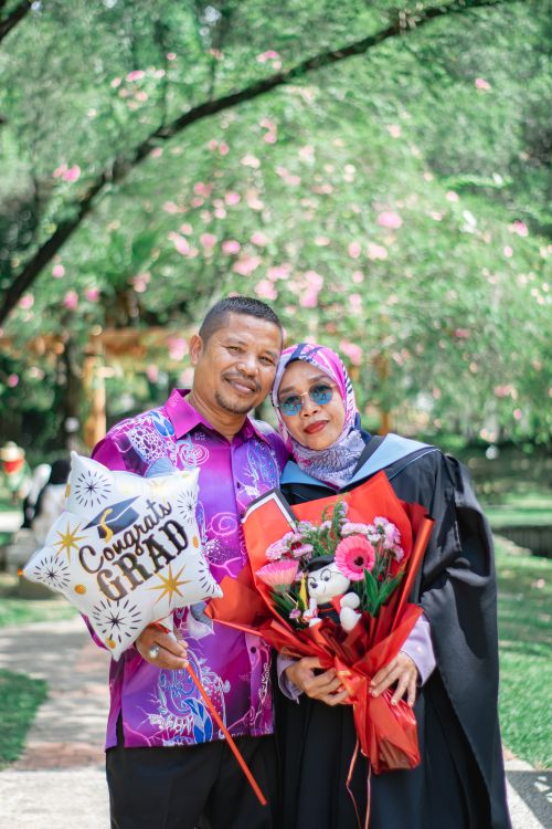 Free Happy couple celebrating graduation with flowers and balloon outdoors. Stock Photo