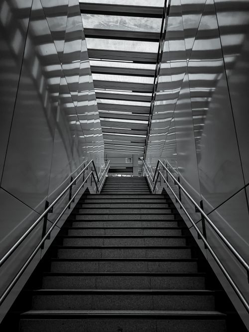 Free Dramatic black and white image of a modern interior staircase with skylight and reflective walls. Stock Photo