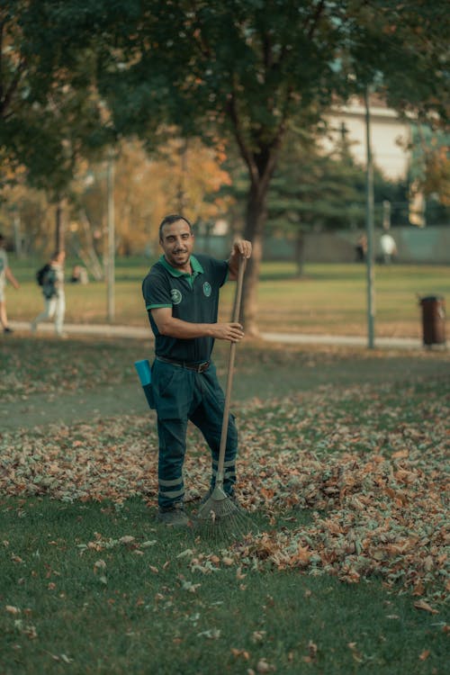 Smiling Worker with Rakes in Park in Autumn