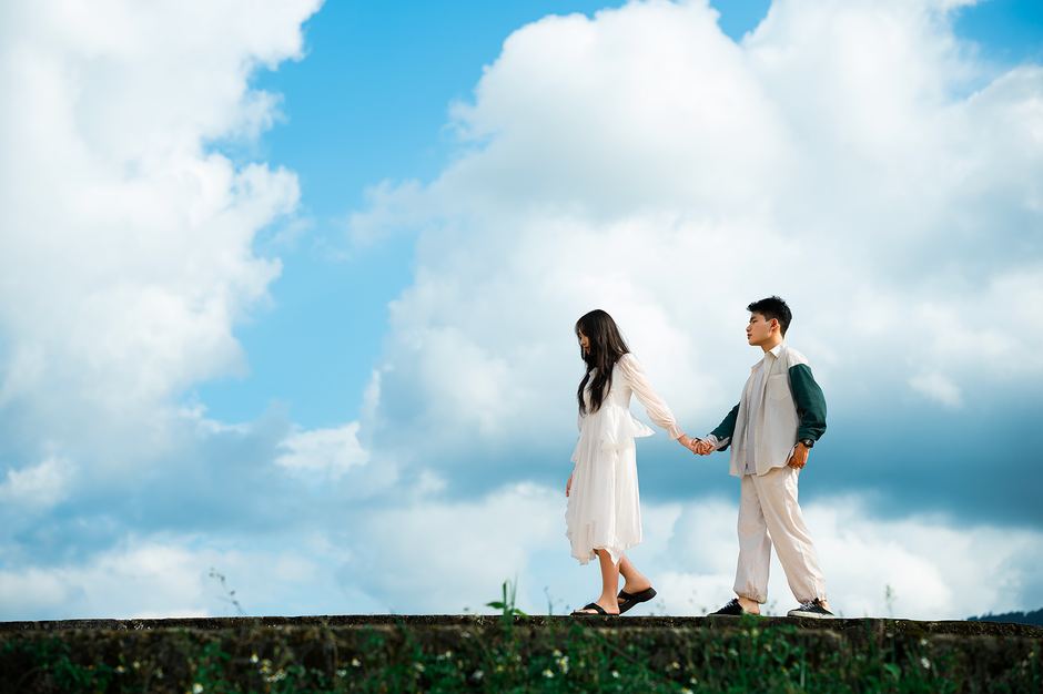 A young couple holding hands and walking outdoors under a bright blue sky in Dalat, Vietnam.