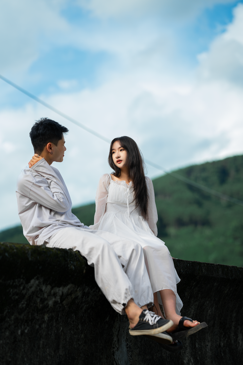 Free Asian couple in white outfits sitting outdoors in Dalat, Vietnam, embracing nature and romance. Stock Photo