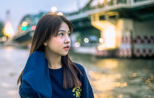 Young Brunette Woman in Sweatshirt on Riverbank in City