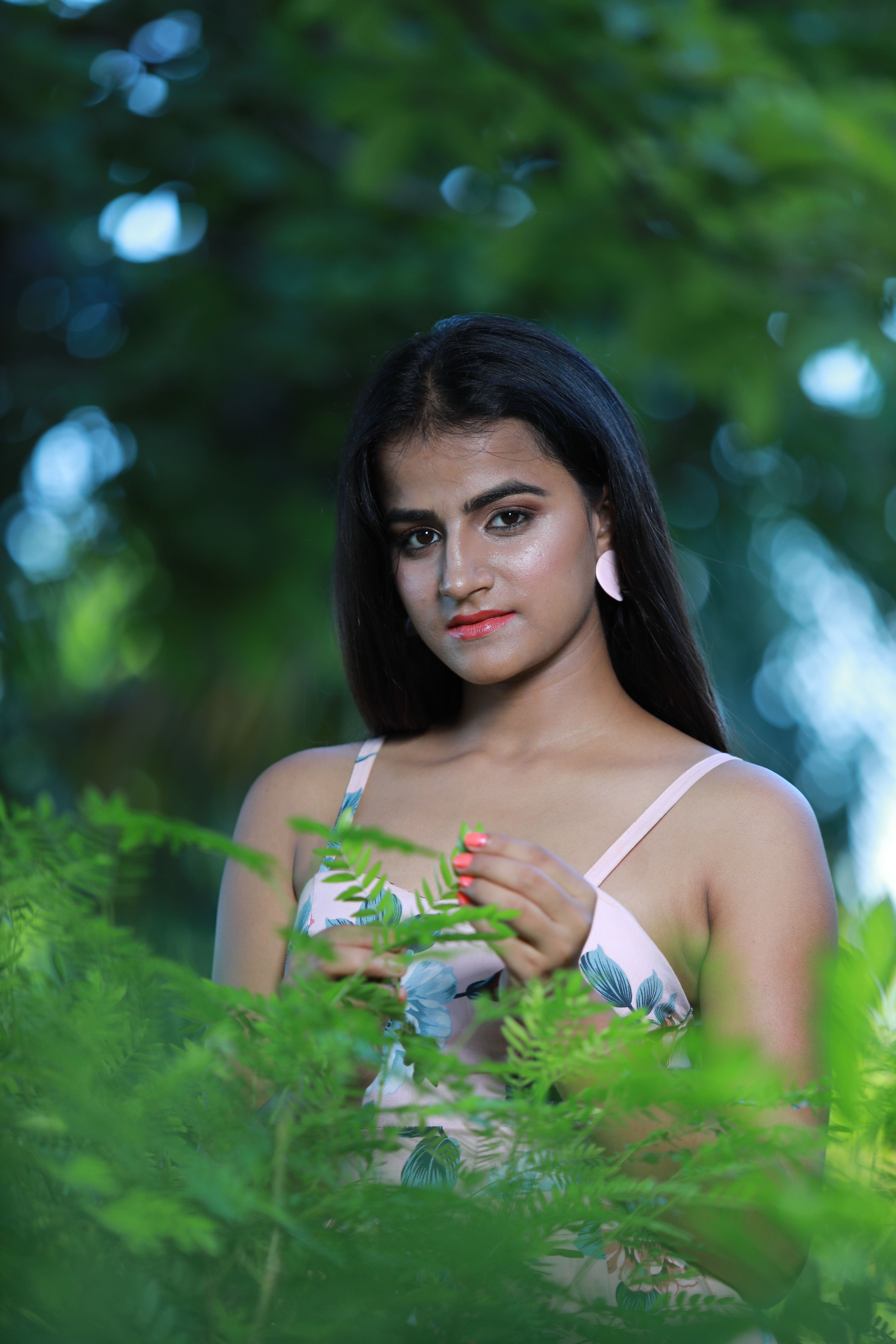 Portrait of a young woman in a floral dress amidst lush green foliage, captured outdoors.