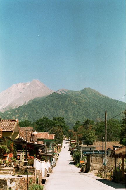 A picturesque village road leading to lush green mountains under a clear blue sky.