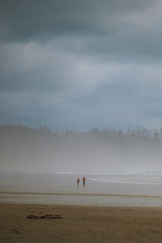 Two figures walk along a misty beach, creating a serene coastal scene.
