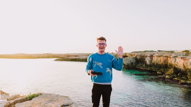 A cheerful man waves from a scenic cliffside in Monopoli, Italy, during sunset.