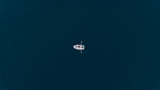 Discover a tranquil aerial view of a solitary rowboat on the open sea near Polignano a Mare.