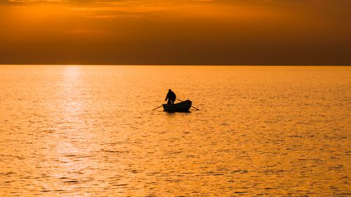 Free A lone figure in a rowboat silhouetted against a golden sunrise over the ocean near Polignano a Mare. Stock Photo