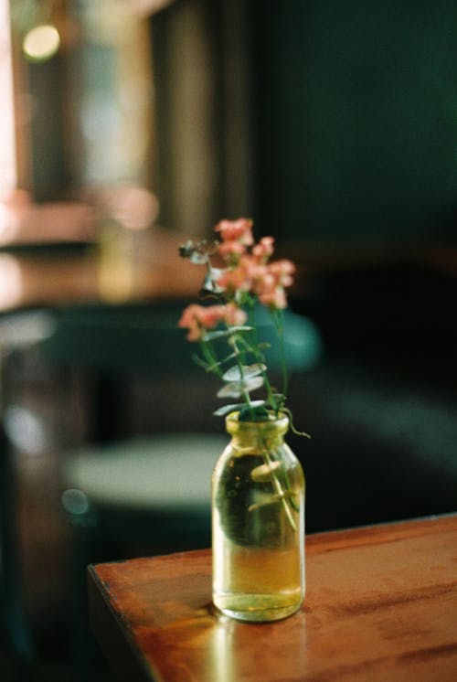 Pink Flowers in a Glass Bottle on the Corner of the Table