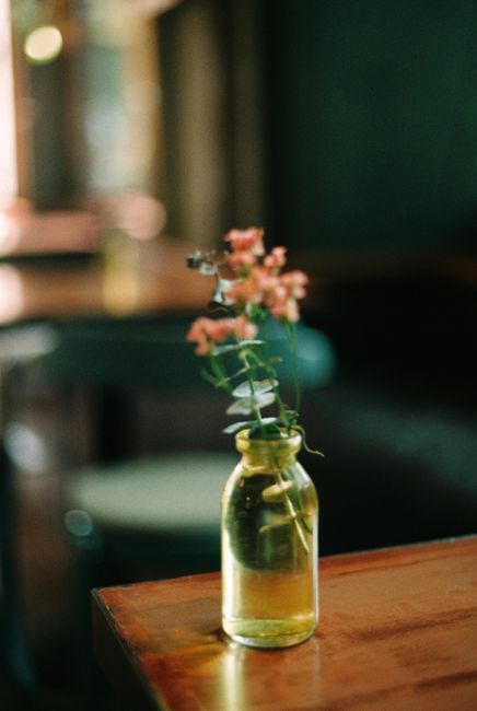 A beautifully composed still life of pink flowers arranged in a glass bottle on a wooden table.