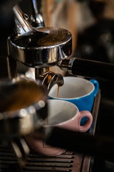 Close-up of espresso pouring into pink and blue cups from a coffee machine.