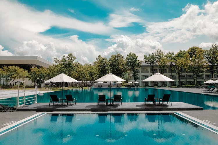 Black Outdoor Lounge Chair In Between Blue Swimming Pool Under White Cloudy Blue Sky