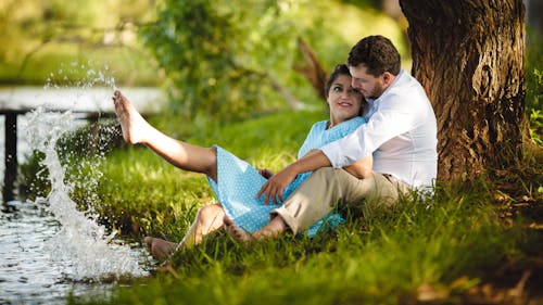 Free Couple Sitting on Grass Under Tree by the River Stock Photo