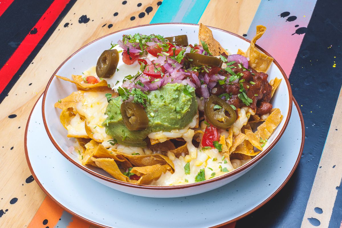 Bowl of nachos with melted cheese, guacamole, jalapeno slices, pickled onion, tomatoes and chili beans