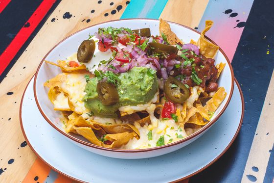 Bowl of nachos with melted cheese, guacamole, jalapeno slices, pickled onion, tomatoes and chili beans