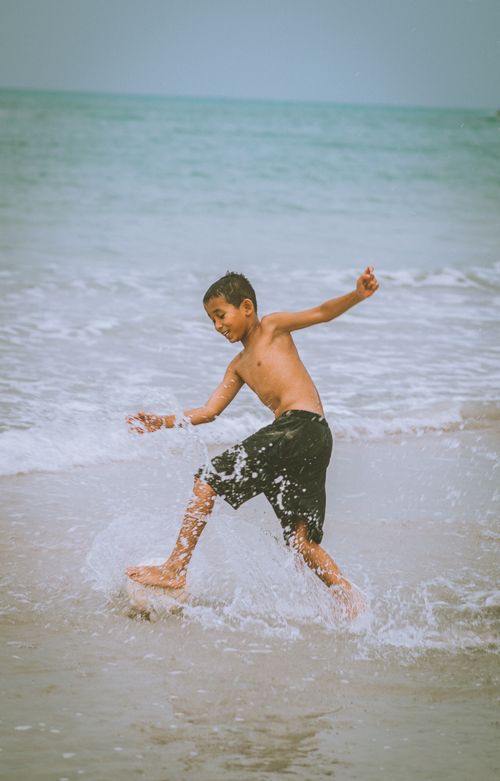 Free A boy enjoys splashing water on a sunny beach in Sungai Liat, Indonesia. Stock Photo