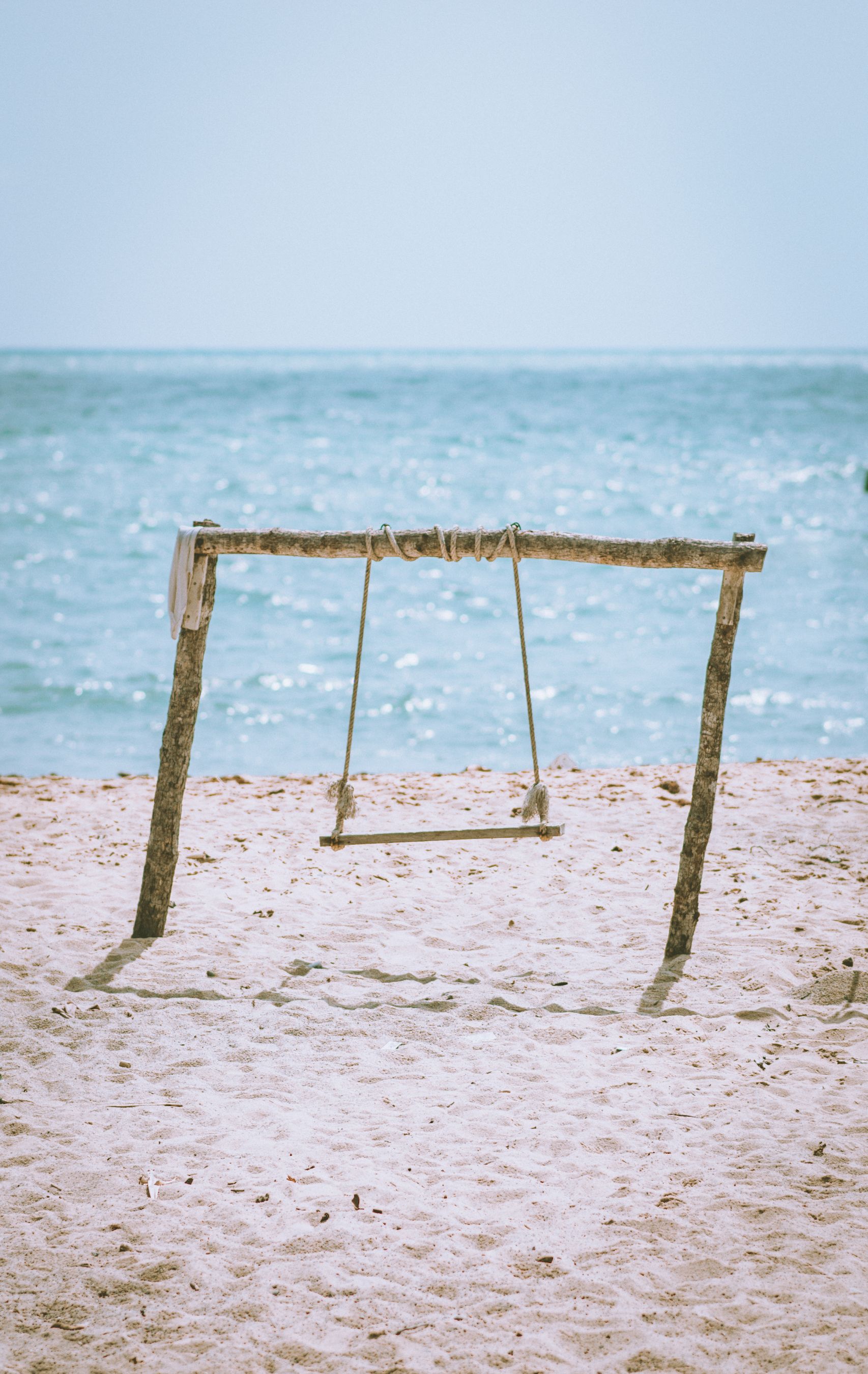 Swing set on a sandy beach overlooking the serene ocean on a sunny day.