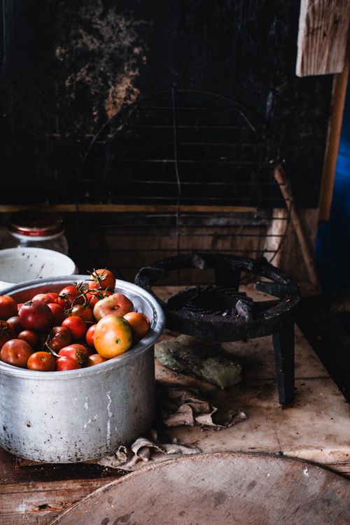 Free A rustic kitchen setup featuring a pot filled with fresh tomatoes alongside an old stove. Stock Photo