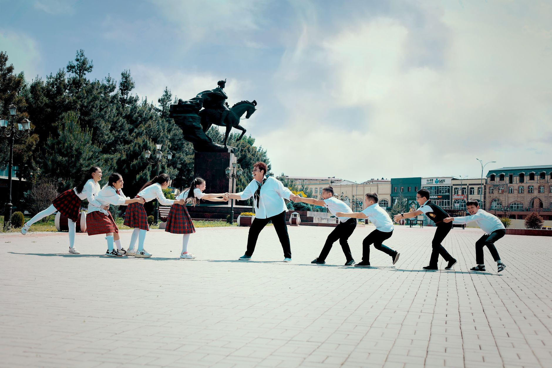 A group of schoolchildren play tug of war by the Babur statue in Navoi Square, Andijan, Uzbekistan.