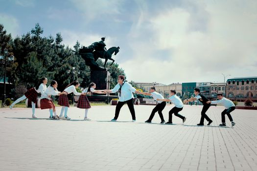 A group of schoolchildren play tug of war by the Babur statue in Navoi Square, Andijan, Uzbekistan.