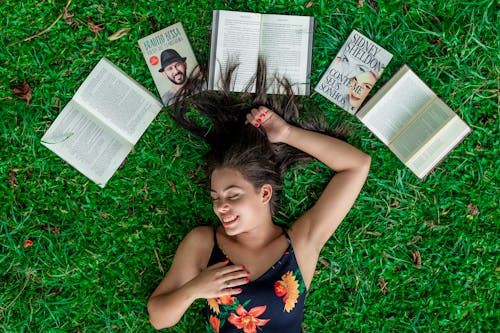 Женщина, лежа на траве возле раскрытых книг