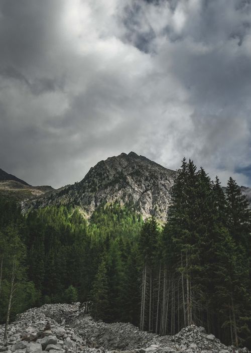 Free Breathtaking mountain view with dense forest and rocky terrain under dramatic skies. Stock Photo