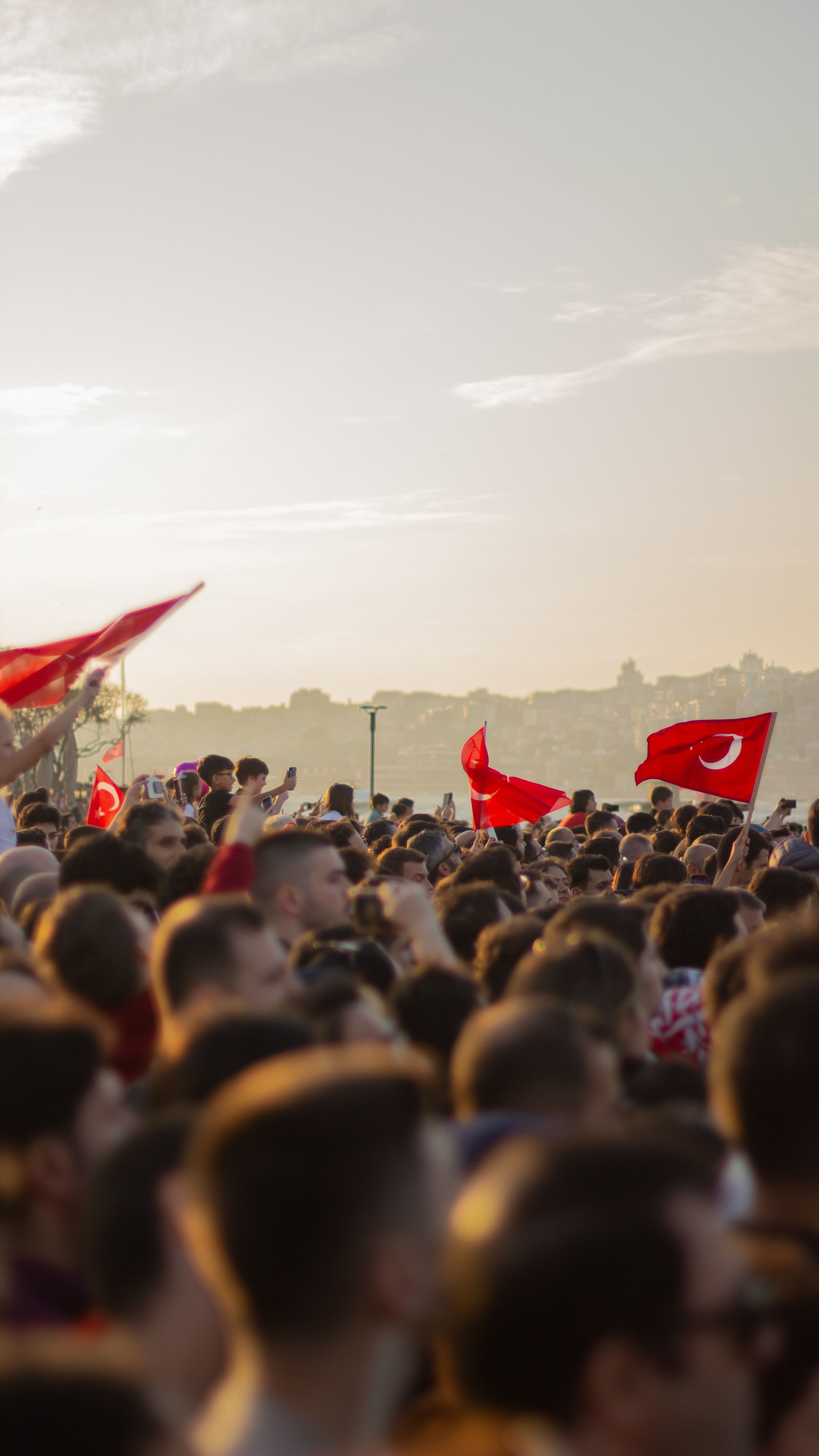 A large crowd gathered outdoors waving Turkish flags during sunset, capturing a lively event atmosphere.