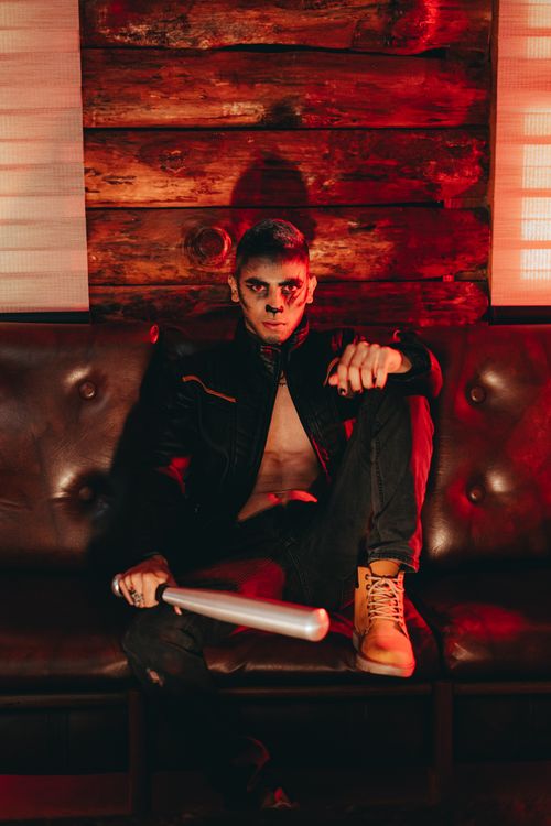 Free Dramatic photo of a man with makeup, holding a bat on a couch with atmospheric lighting. Stock Photo