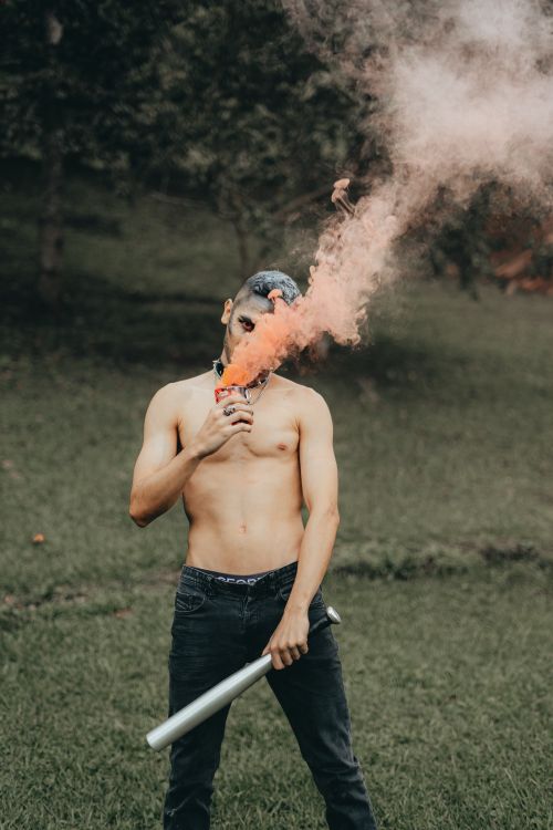 Free A shirtless man holding a smoke flare stands in a grassy field, creating a dramatic scene. Stock Photo