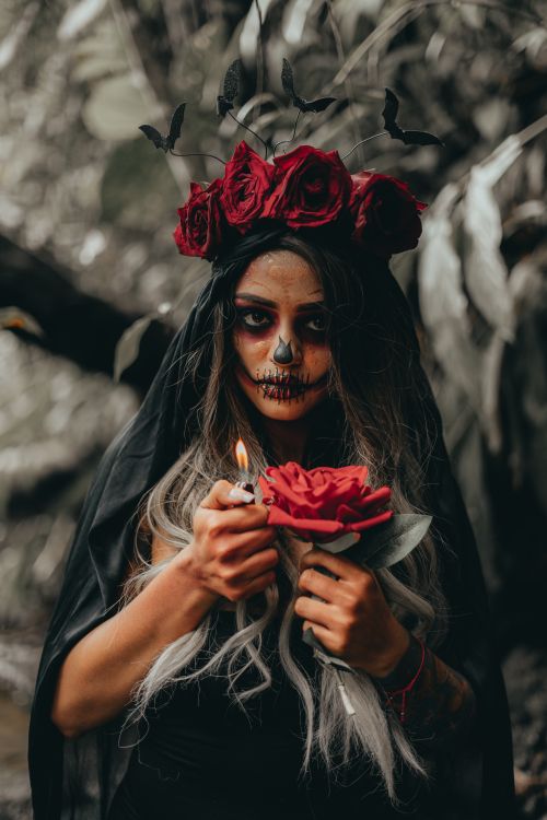 Free Mystical portrait of a woman in Day of the Dead makeup with red roses and candle. Stock Photo