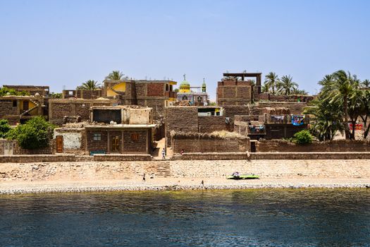 Charming view of a traditional village with historic architecture on the Nile Riverbank under a clear blue sky.