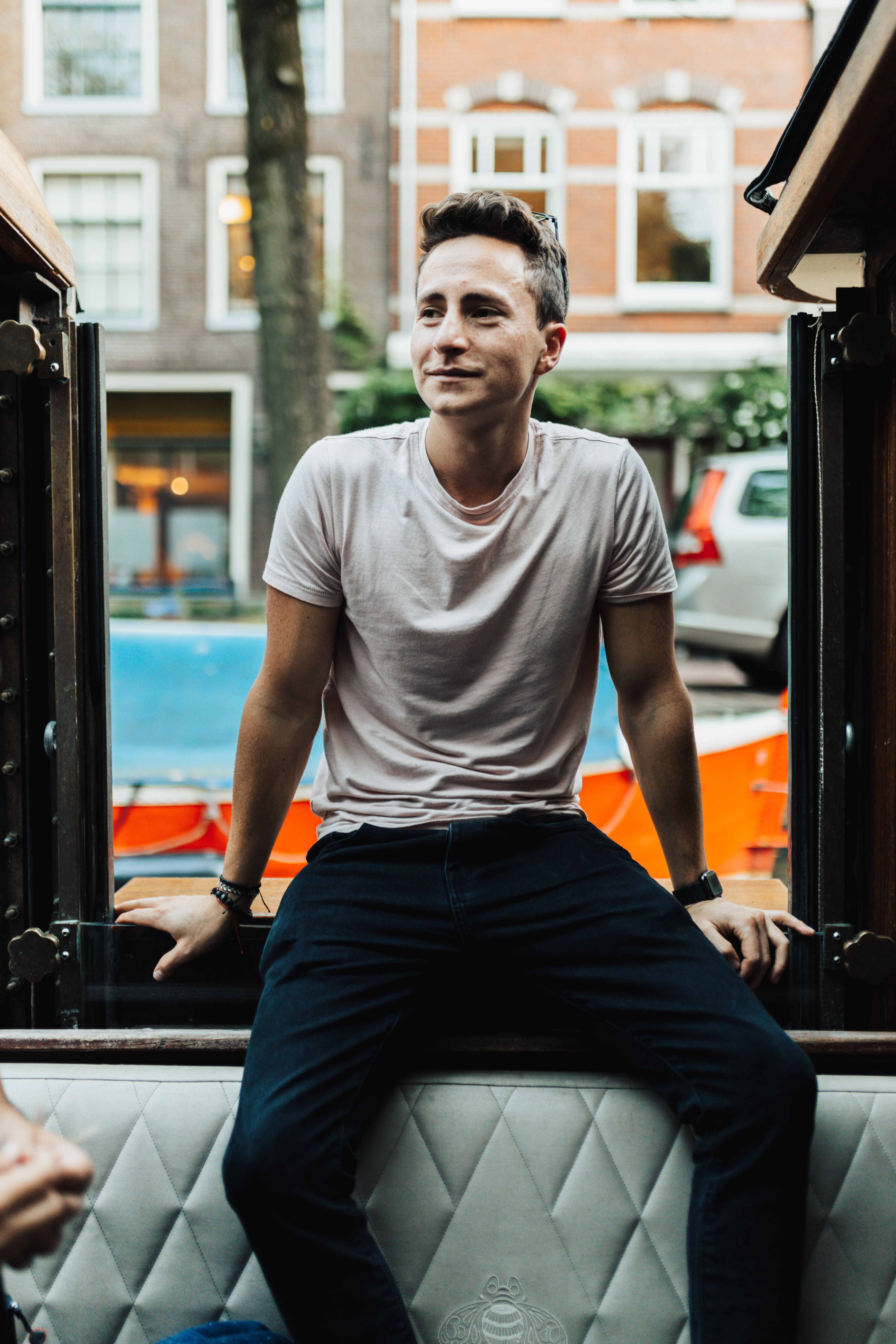 A man with short hair and t-shirt smiling while sitting in an urban environment.