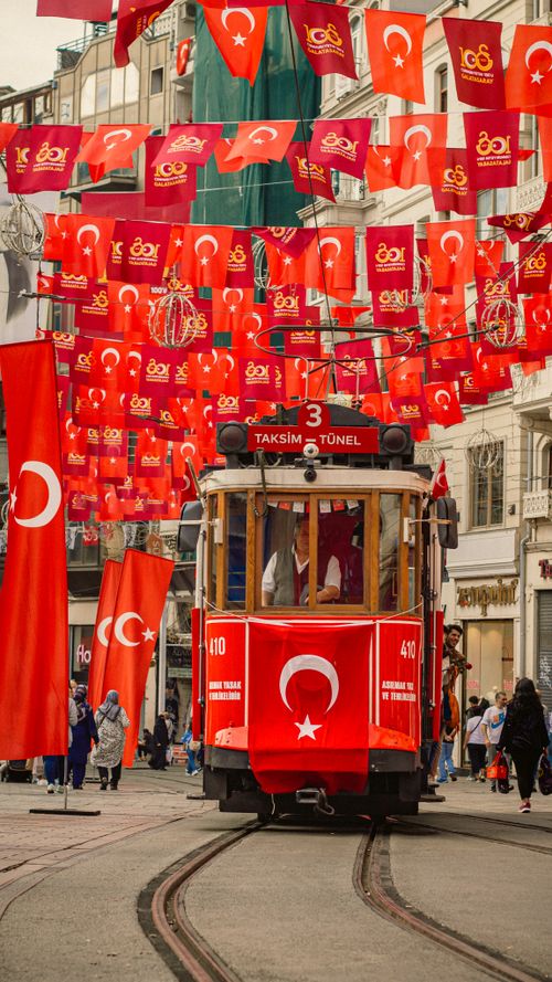 Free Historic Taksim tram surrounded by vibrant Turkish flags in Istanbul's bustling street. Stock Photo
