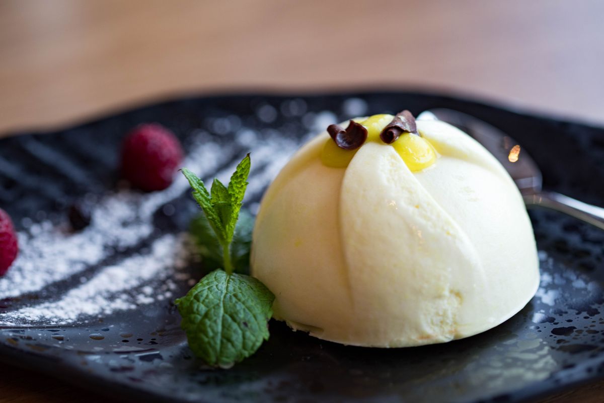 White semifreddo dome with lemon curd center and chocolate curls, mint and raspberries on dark plate