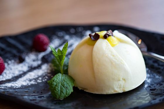 White semifreddo dome with lemon curd center and chocolate curls, mint and raspberries on dark plate