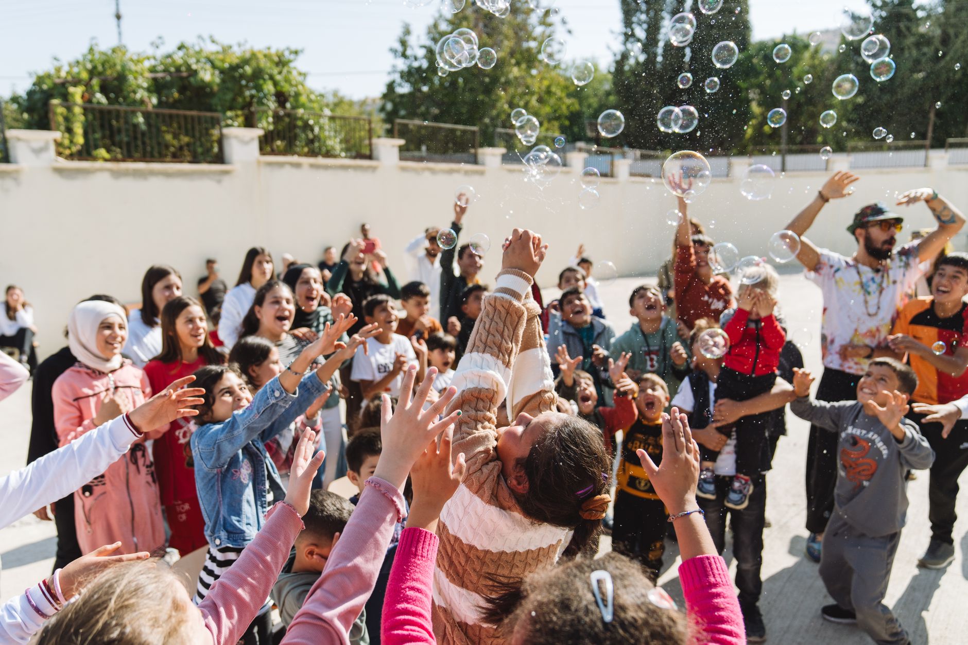 juggler for kids party cairo — Group of excited children and adults celebrating with soap bubbles outdoors in daylight.