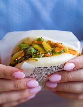 Delicious bao bun filled with fresh vegetables held by hands with pink nails.