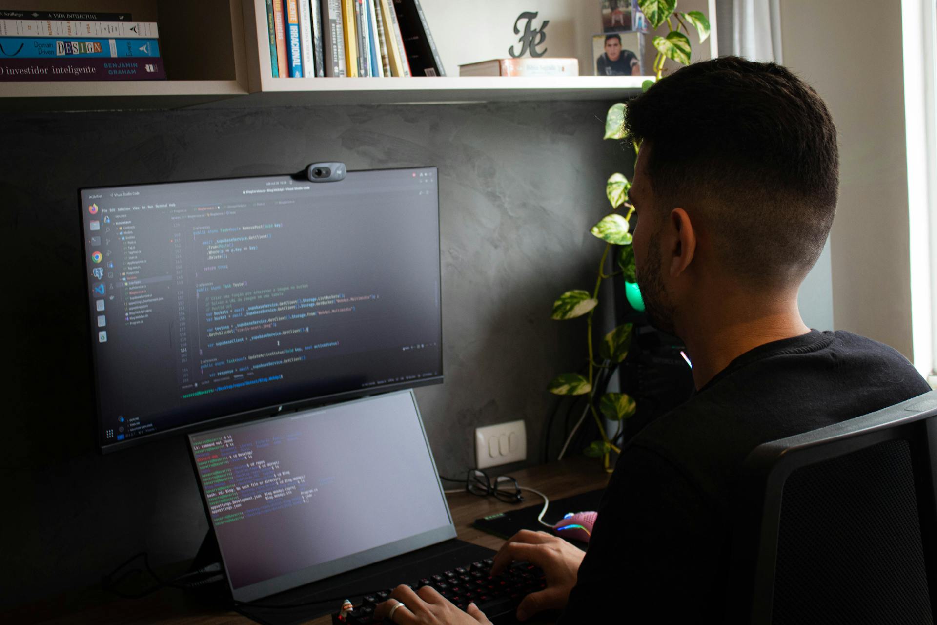 A programmer coding on a laptop and monitor in a stylish office setup.