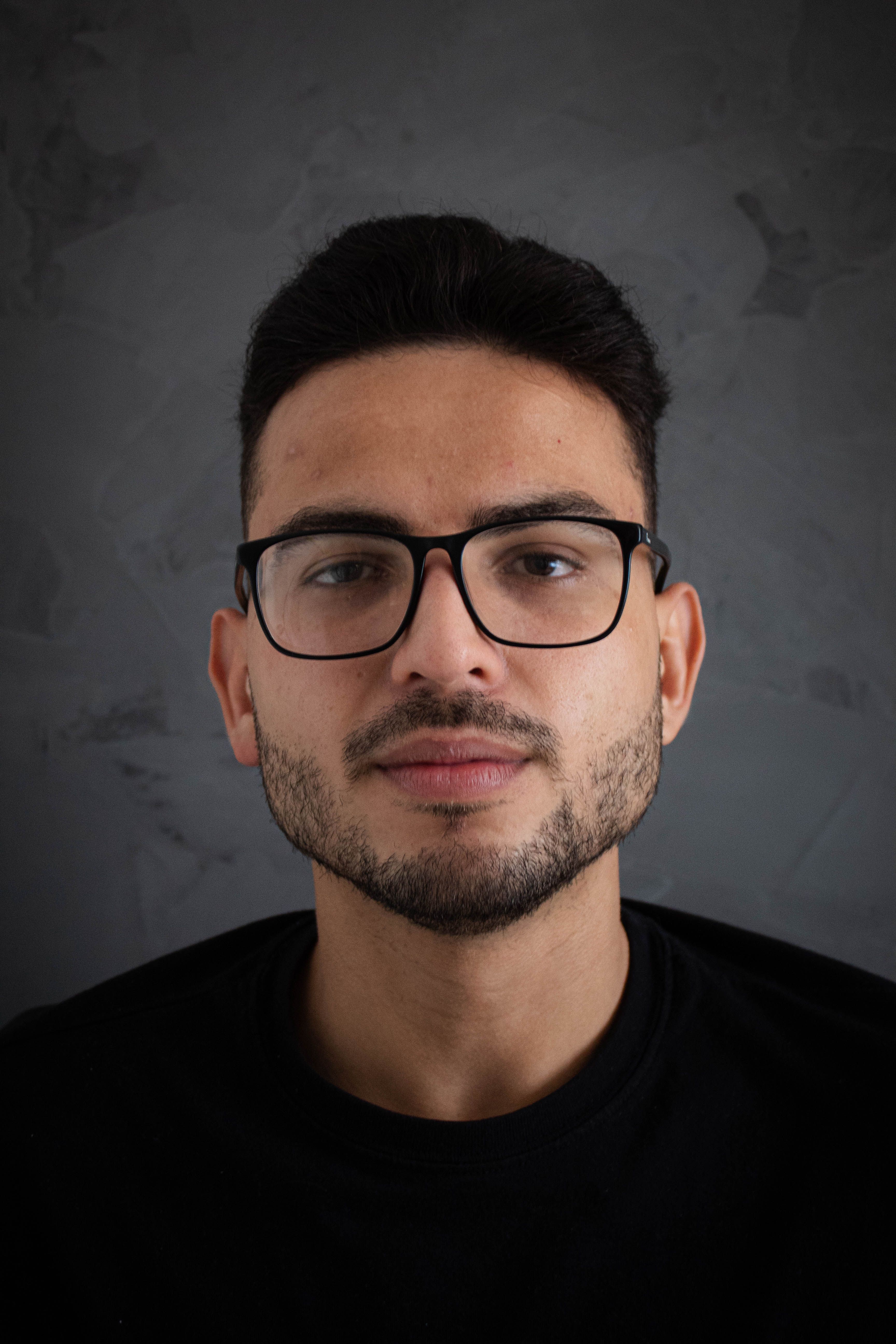 Close-up portrait of a young man with eyeglasses against a gray textured backdrop.