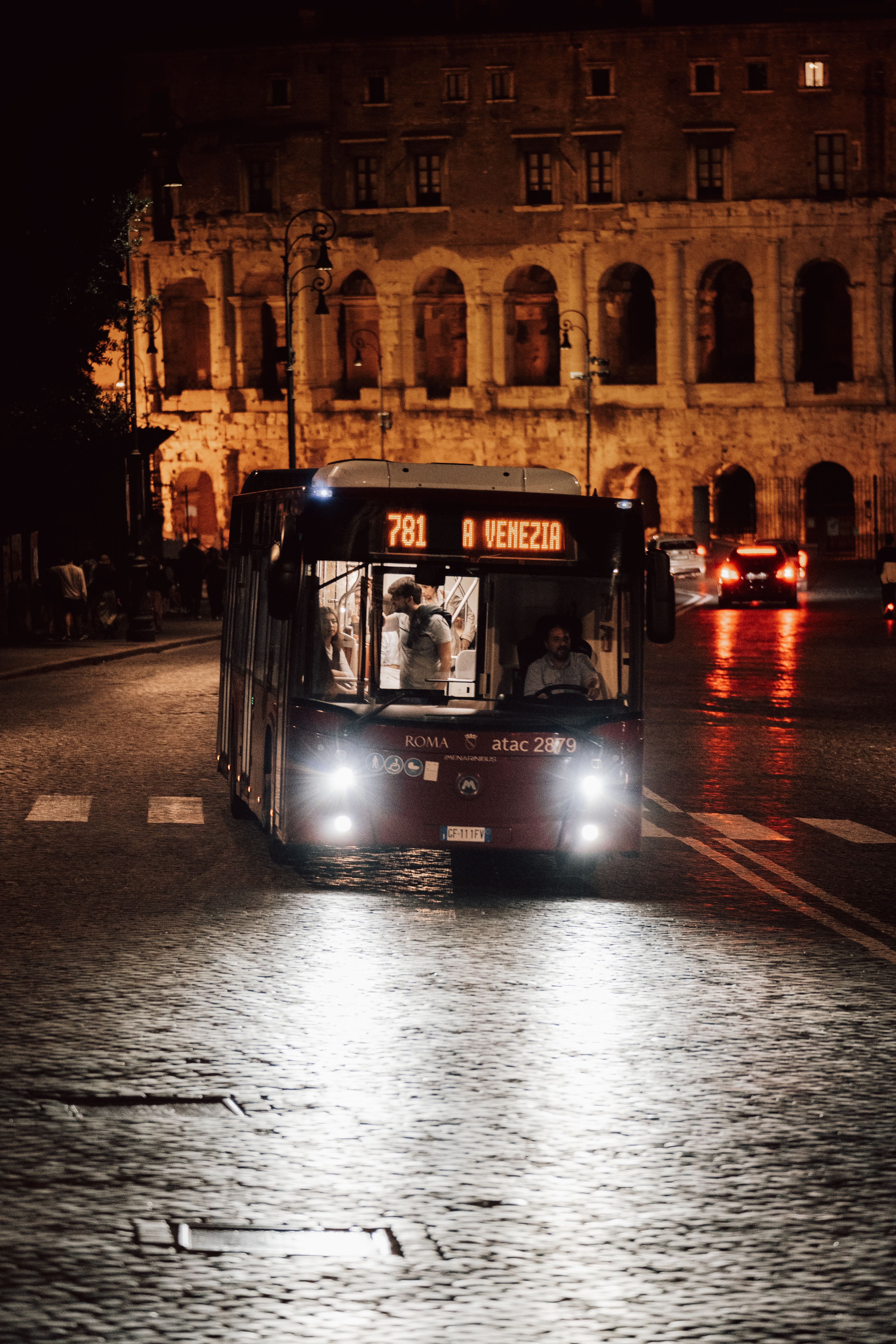 A city bus passes by the illuminated Colosseum in Rome, capturing the vibrant urban night atmosphere.