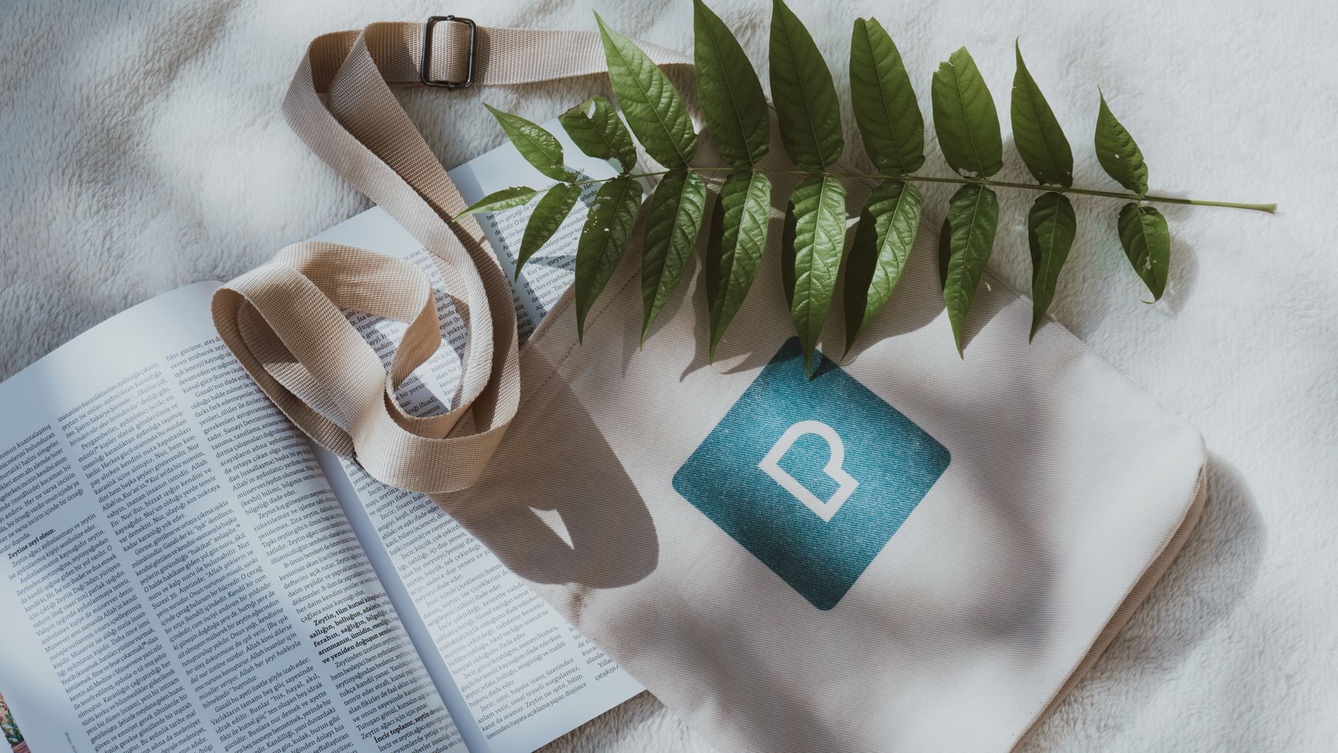 Modern flat lay image featuring a book, leaf, and stylish tote bag on a textured surface.