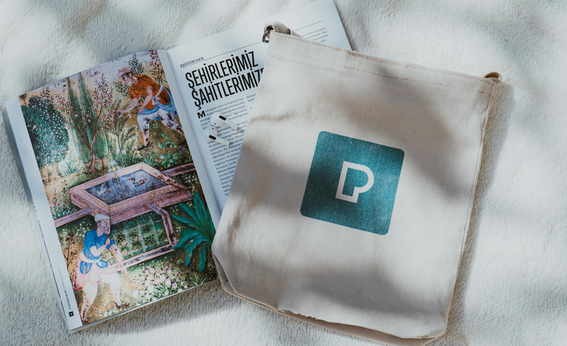 A decorative open book and a tote bag with a logo on a soft textured backdrop.